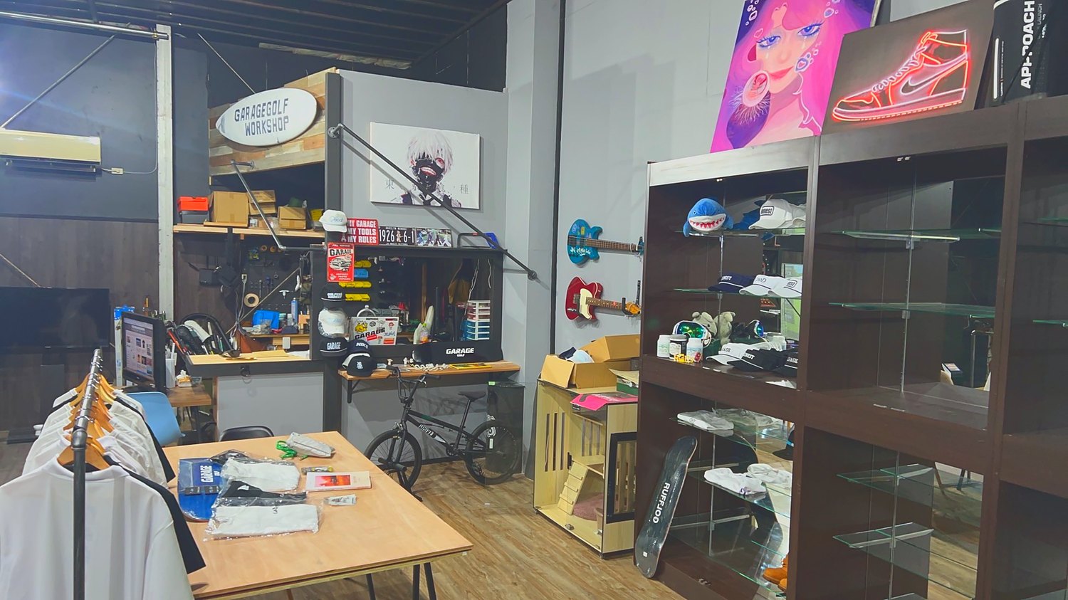 ショップの店内。ウェアとキャップの棚。壁の飾りにネオンサイン、BMX、ギター、アートのキャンバス